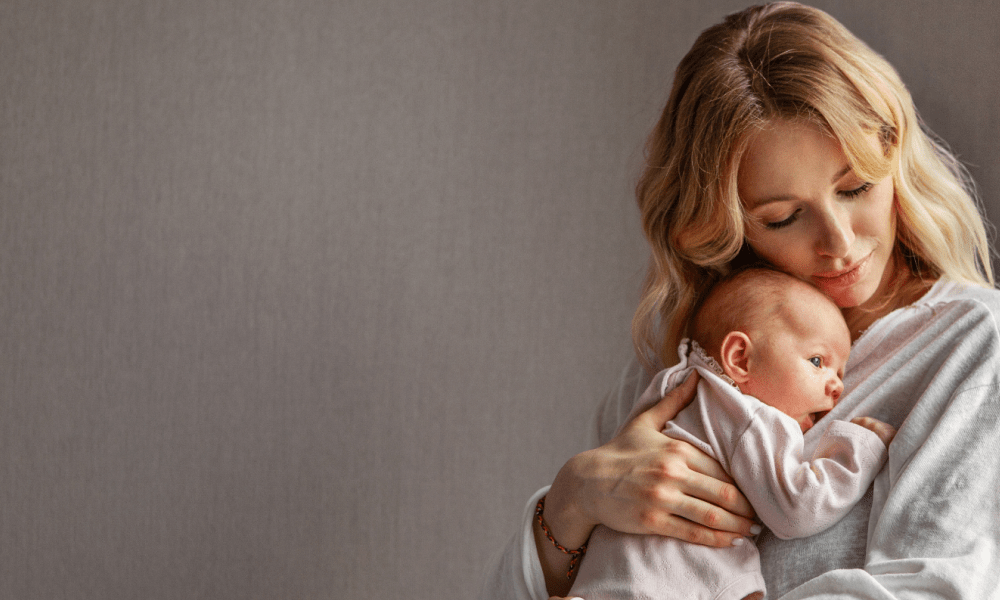 A mother with blonde wavy hair tenderly cradles her newborn baby against her chest, embodying the peace of mind Babysense video baby monitors provide for parents