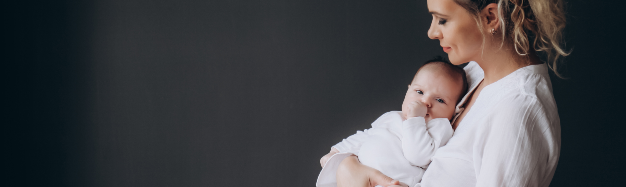 A smiling mother with blonde hair tied in a high ponytail holds her infant dressed in a white onesie, showcasing an hd video baby monitor for her child