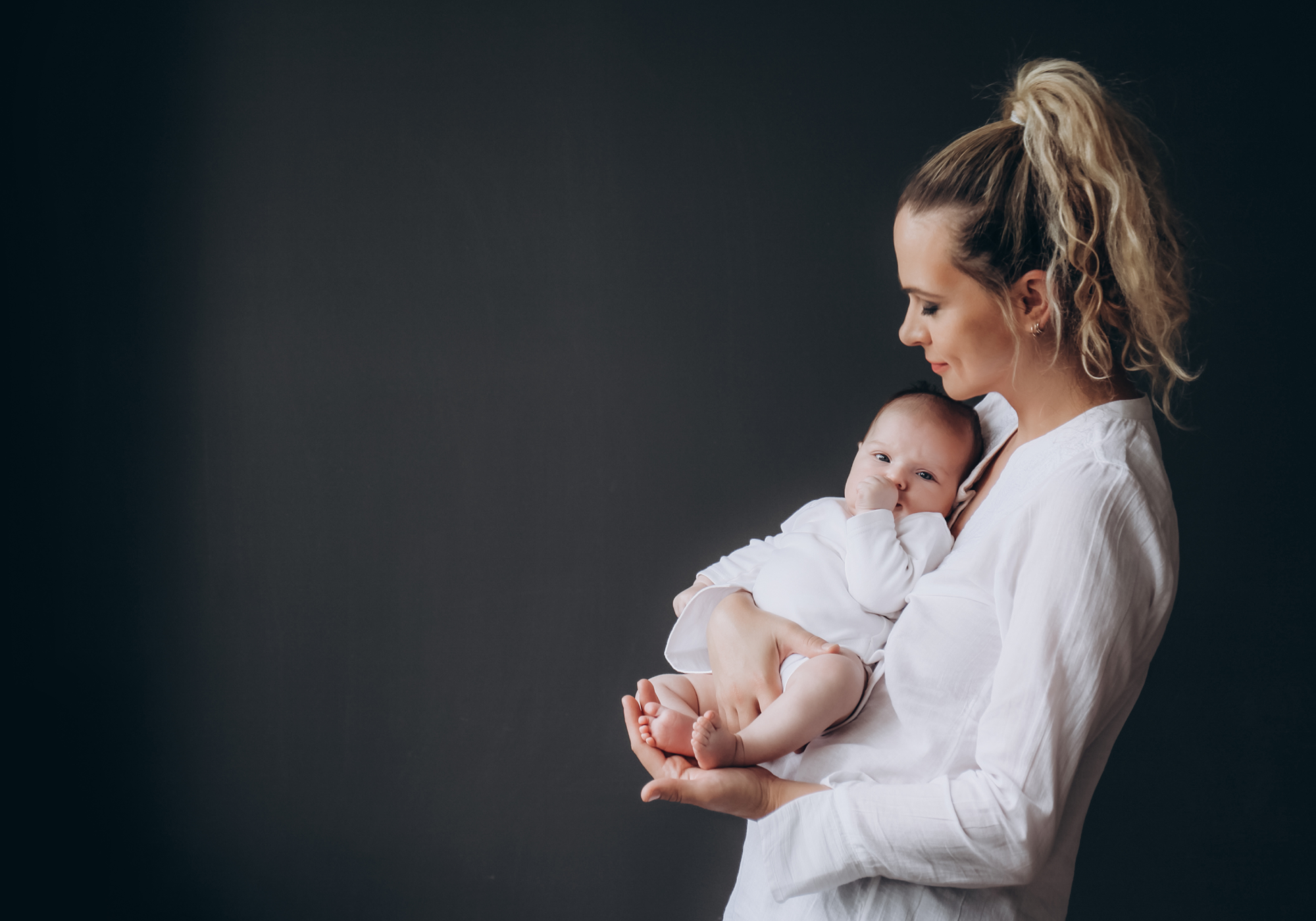 A smiling mother with blonde hair tied in a high ponytail holds her infant dressed in a white onesie, showcasing an hd video baby monitor for her child