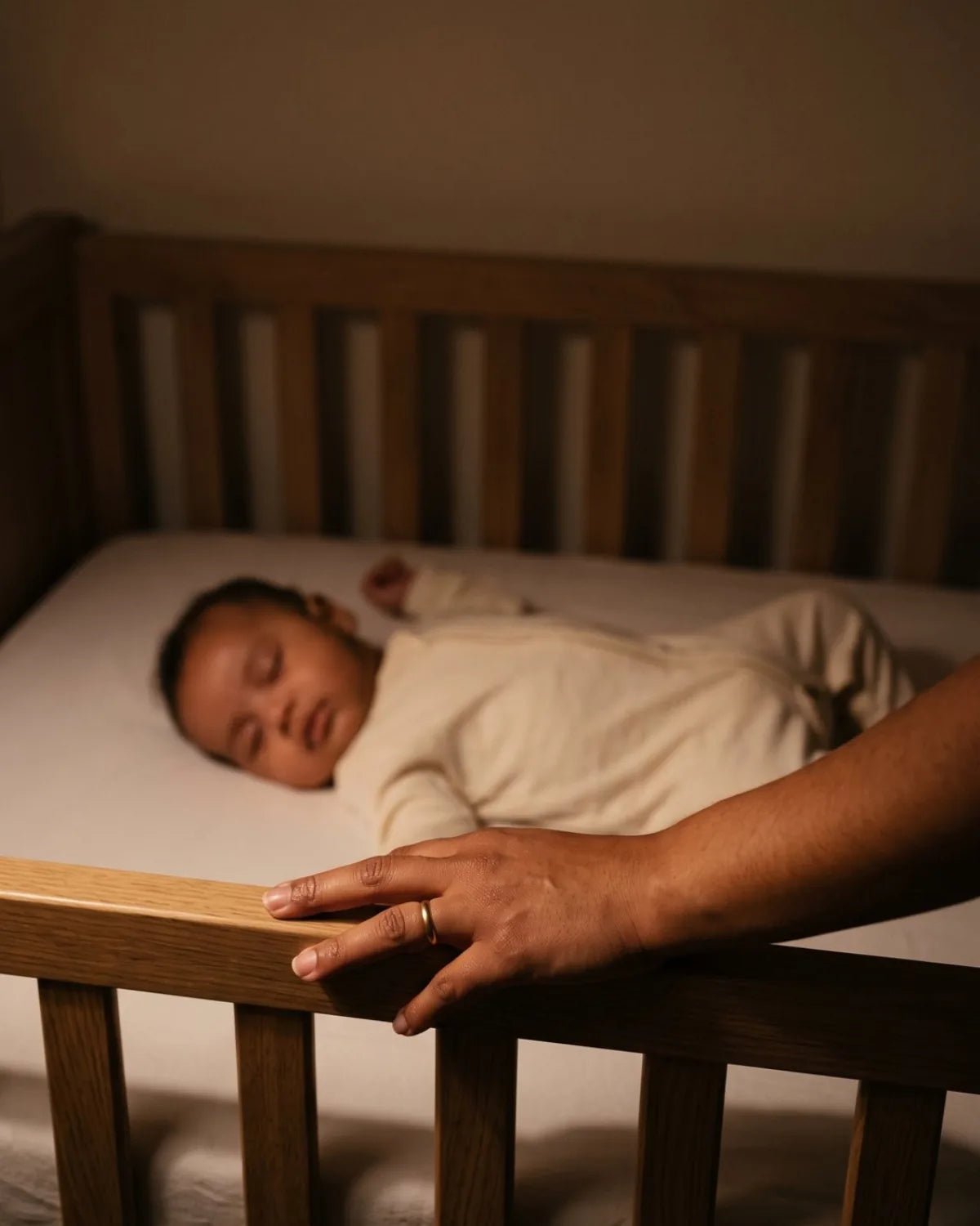 Parent's hand resting on the crib rail while a baby sleeps at night
