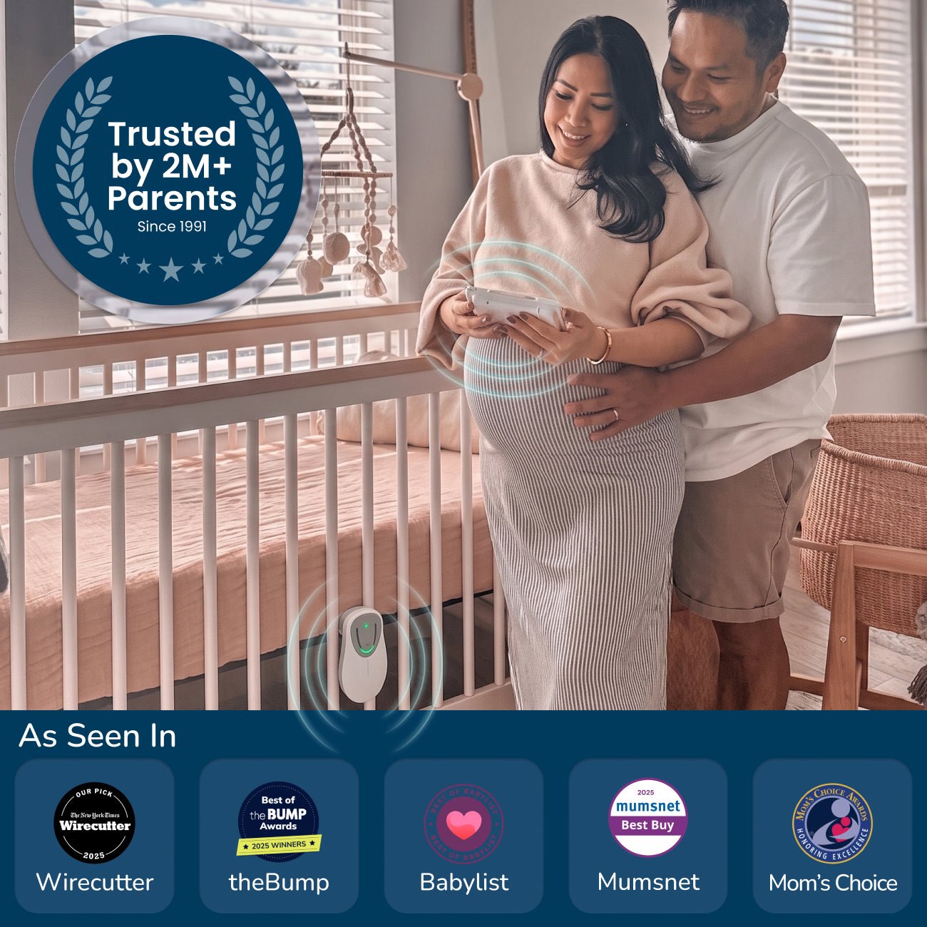 A happy expectant couple stands in a nursery, with the pregnant woman holding a monitor to her belly, showcasing an HD video baby monitor with a white crib and baby motion sensor in the background